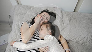 The daughter hugs her mother lying together on the bed and communicating on a mobile phone with relatives while in self