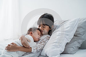 Daughter kid with infant sibling playing on bed wearing white