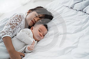 Daughter kid with infant sibling playing on bed wearing white