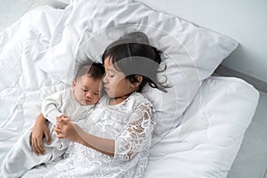 Daughter kid with infant sibling playing on bed wearing white