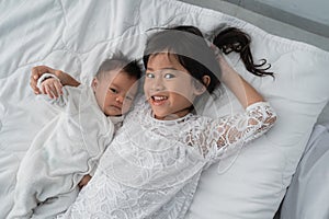 Daughter kid with infant sibling playing on bed wearing white