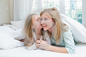 Daughter kissing her mother on the cheek in the bed