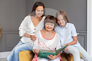 Daughter, moter and grandmother sit in chair with photoalbum in hands