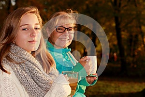 Daughter and mother drink tea in autumn park