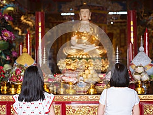 Daughter and mother pay respects to Buddha statue in Chinese shrine