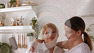 Daughter and old mother dressed in white shirts hug in the kitchen at home.