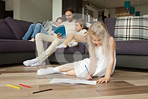 Daughter playing on floor while parents and son reading book