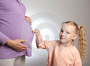 The daughter points to the big belly of the pregnant mother. The concept of waiting for replenishment in the family