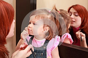 Daughter powders, mother makes make-up near mirror