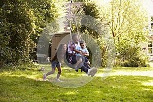 Daughter Pushing Father And Son On Tire Swing In Garden