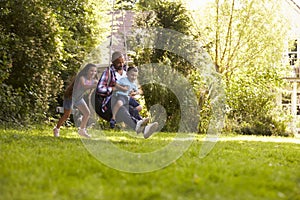 Daughter Pushing Father And Son On Tire Swing In Garden