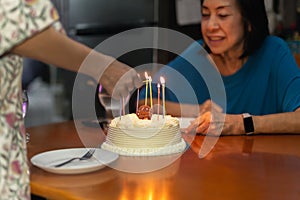Daughter& x27;s hand lighting candles on senior with other birthday cake.