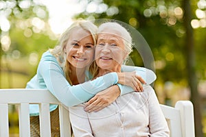 Daughter with senior mother hugging on park bench photo