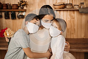 The daughter of seven years old and the son of eleven years old hug mom. Masked family in quarantine at home