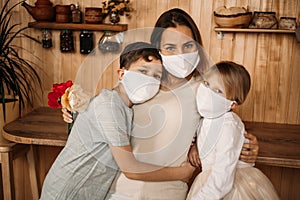 The daughter of seven years old and the son of eleven years old hug mom. Masked family in quarantine at home