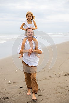 Daughter sitting on father`s shoulders. Father and daughter playing together at the beach. Happy family. Having fun together.