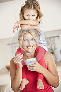 Daughter Sitting On Shoulders Whilst Mother Eats Yoghurt