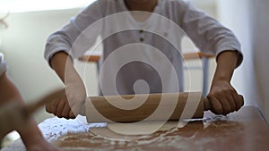 Daughter and a son are all in white T-shirts at the same table preparing a pie. weekends with family. boy and girl roll