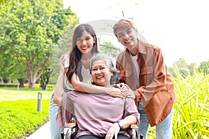 Daughter and son bring elderly mother in wheelchair to breathe fresh air at outdoor par