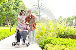 Daughter and son bring elderly mother in wheelchair to breathe fresh air at outdoor park.