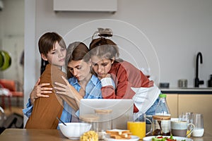 Daughter and son hug mom in kitchen. Sad single mother has problems with online work