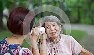 Daughter talking to hearing impaired elderly woman , using paper tube