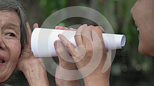Daughter talking to hearing impaired elderly woman, using paper tube
