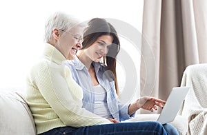 Daughter teaching her elderly mother using laptop