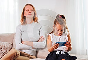 Daughter using a smartphone, while frustrated mother is watching her