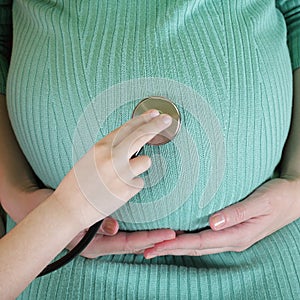 Daughter using stethoscope  white examining pregnant mother