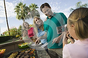 Daughter (7-9) video taping parents grandmother sister (7-9) at outdoor barbecue. photo