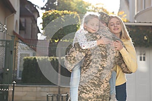 Daughter and wife hugging soldier in Ukrainian military uniform outdoors, space for text. Family reunion