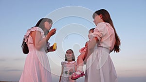 Daughters and mother are blowing bubbles in the park at sunset. Slow motion. Happy mother playing with children blowing