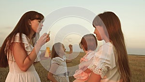 Daughters and mother are blowing bubbles in the park at sunset. Slow motion. Happy mother playing with children blowing