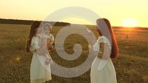 Daughters rejoice and smile, bubbles fly in park at sunset. Slow motion. Happy mother playing with children blowing soap