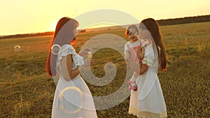 Daughters rejoice and smile, bubbles fly in park at sunset. Slow motion. Happy mother playing with children blowing soap