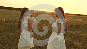 Daughters rejoice and smile, bubbles fly in park at sunset. Slow motion. Happy mother playing with children blowing soap