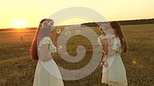 Daughters rejoice and smile, bubbles fly in park at sunset. Slow motion. Happy mother playing with children blowing soap