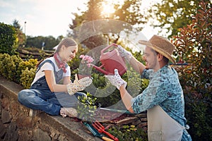 Daugther and father working together in the flower garden outdoors, girl holding a flower pot, man watering it with watercan photo