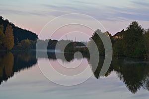 Dawn in the forest near the lake. The forest is reflected in the water. Autumn Early morning. Russia