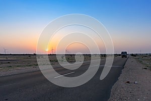 Dawn light in desert sky with empty road passing through the desert. Wind mills in the horizon, Sun rise at Thar desert, Rajasthan