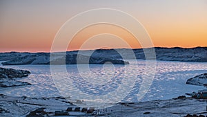 Dawn over a frozen lake. The sky above the ridge is colored orange.