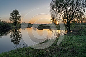 Dawn over the lake. Beautiful evening blue sky at sunset with flaming bright light clouds. Warm summer evening at sunset. May