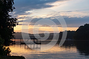 Dawn over Lake Lanier; silhouette of a dock and trees on a lake under a purple and orange sky with clouds photo