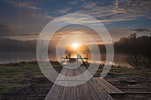 dawn over a misty lake with a wooden pier in the forest in morning