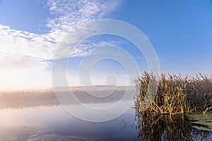 Dawn over the river on a summer morning, fog over the field, grass with hoarfrost