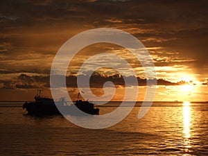 Dawn at sea showing a warm yellow glow on the skies and a fishing boat