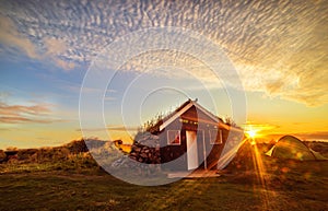 Dawn on the shore of the Atlantic Ocean. A traditional old house with a roof overgrown with grass and a tent on the beach. Iceland