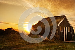 Dawn on the shore of the Atlantic Ocean. A traditional old house with a roof overgrown with grass and a tent on the beach. Iceland