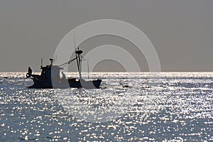 Day in the atlantic ocean. Silhouette of a fishing schooner and glare of bright light on the waves. A lot of sun